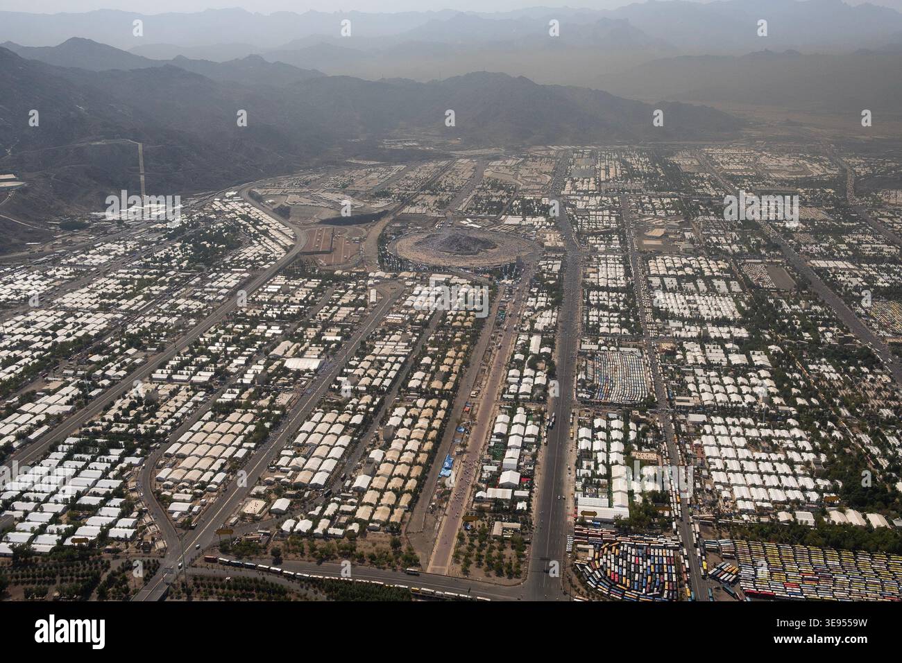 Eine weitläufige urbane Landschaft voller Reihen weißer Zelte und temporärer Bauten, umgeben von fernen Bergen unter einem trüben Himmel. Stockfoto