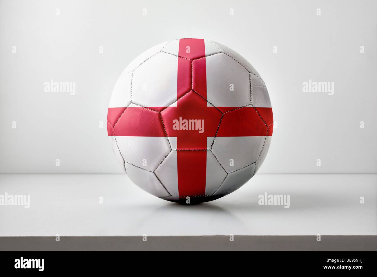 Ein Fußball mit Englands rotem Kreuz auf weißem Hintergrund, zentral platziert mit sanfter Beleuchtung und minimalem Studio-Setup. Stockfoto