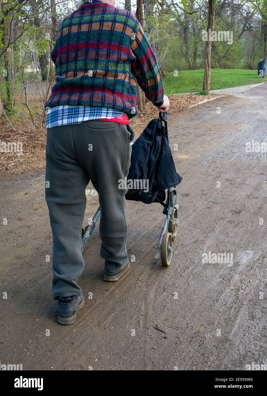 Ein alter Mann läuft mit einem Rollator im Regen durch den Park Stockfoto
