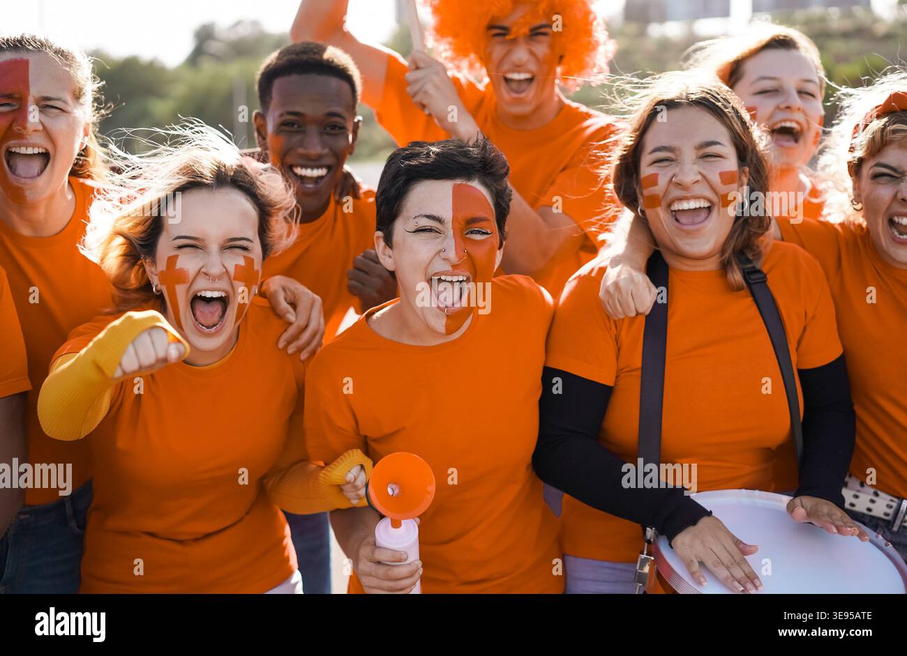 Orange Sportfans haben Spaß beim Support ihrer Mannschaft - Fußballfans haben Spaß bei der Wettkampfveranstaltung - Hauptfokus auf das Gesicht des mittleren Mädchens Stockfoto
