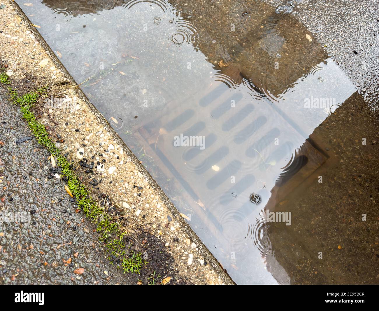 Regenwasser fließt aus der verstopften Ablaufabdeckung nach oben Stockfoto