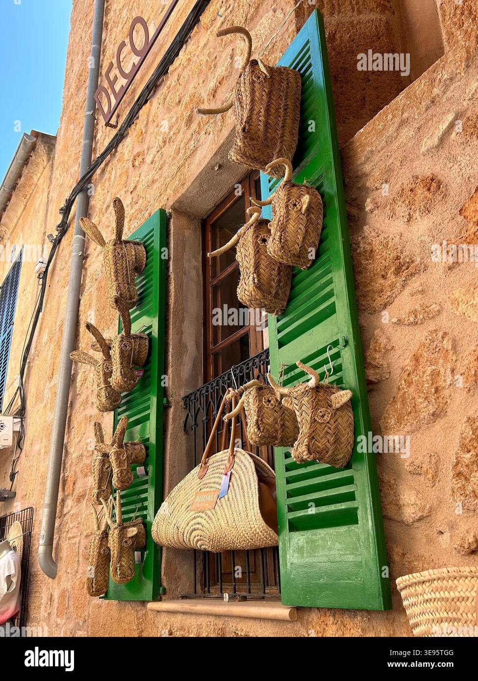 Ein Schaufenster auf Mallorca zeigt handgefertigte Strohsäcke und dekorative Kuhköpfe als traditionelle Souvenirs. Die rustikale Fassade mit grünem Holzladen - Smartphone-aufgenommenes Stockfoto