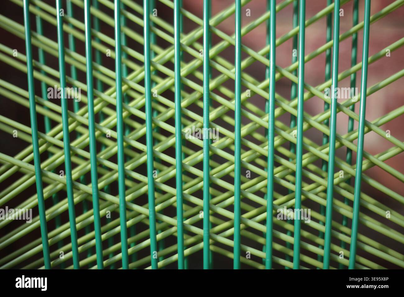 Nahaufnahme eines Gartenstuhls aus grünem Drahtgeflecht mit Kreuzgittermuster, abstraktem geometrischem Hintergrund mit geringer Schärfentiefe. Stockfoto