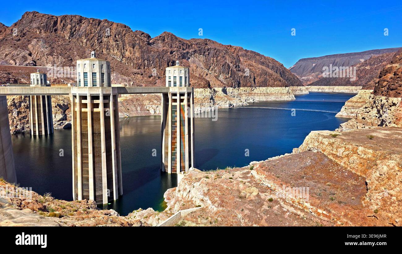 Der Hoover-Staudamm ist über dem Lake Mead. Malerische Aussicht auf die Einzugstürme des Hoover Dam, die sich vom Lake Mead erheben, mit Wüstenbergen, exponierter Küste und Stockfoto