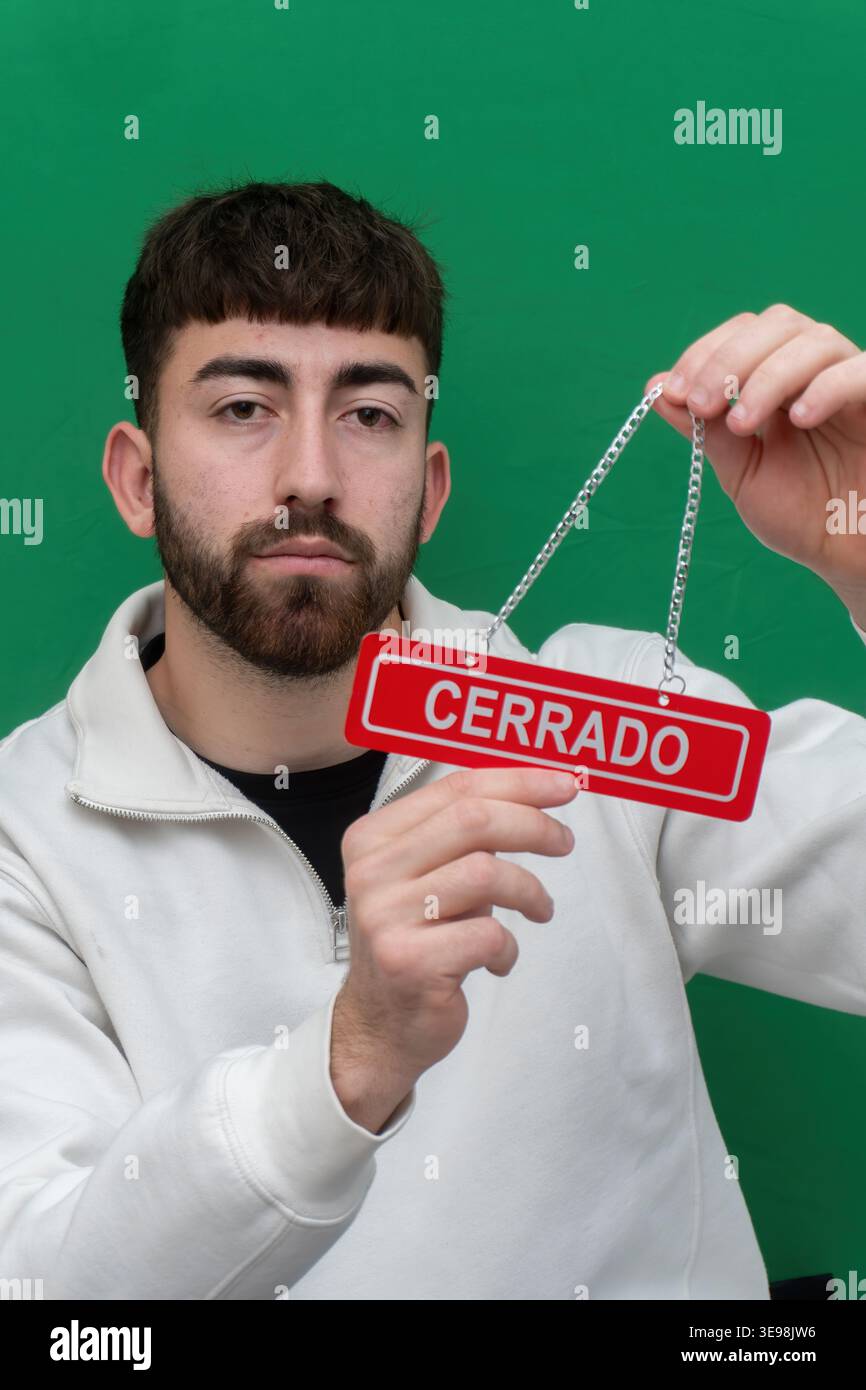 Mann mit rotem Cerrado-Schild, das anzeigt, dass ein Unternehmen geschlossen ist oder nicht verfügbar ist, mit einem grünen Hintergrund Stockfoto