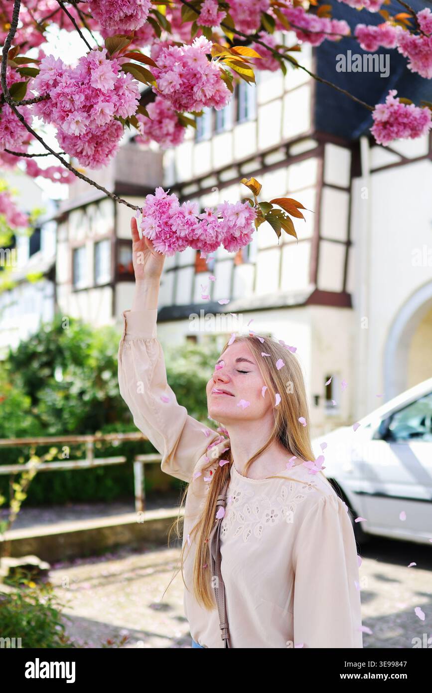 Modische Frau im Pastelloutfit unter blühendem Baum, saisonale Schönheit und Lifestyle-Konzept. Stockfoto
