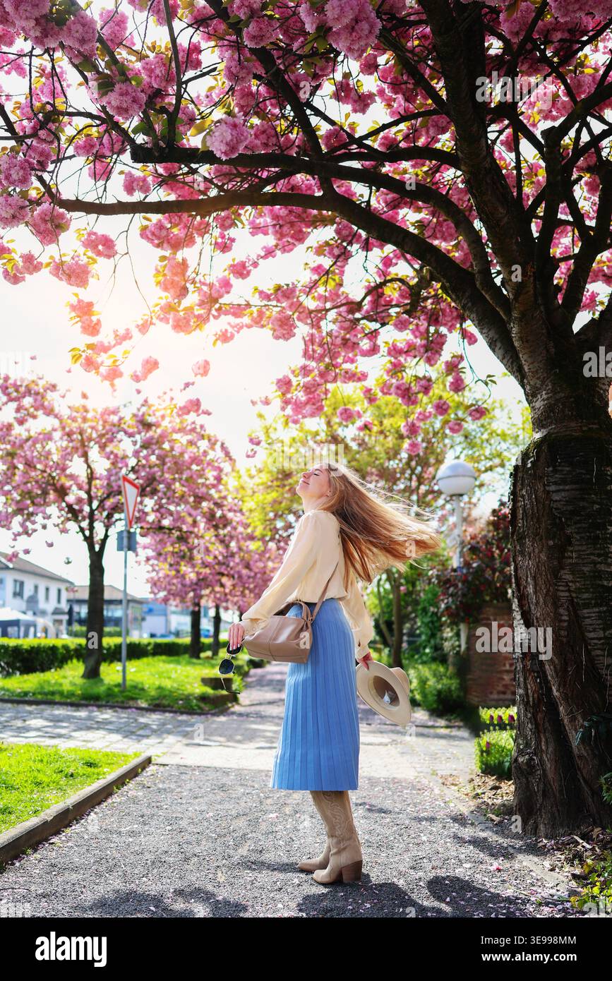 Junge Frau, die unter Sakura-Bäumen läuft, sonniger Frühlingstag und friedliche Naturstimmung. Stockfoto