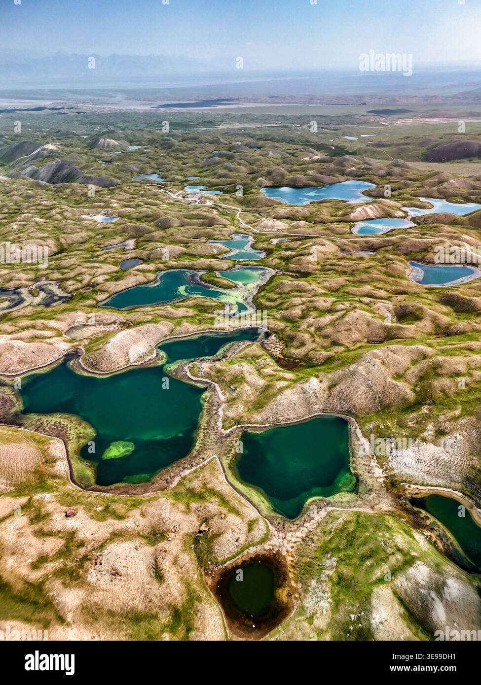 Blick aus der Vogelperspektive auf den Tulpar Lake mit seinem türkisfarbenen, alpinen Wasser, das über die sanften grünen Hügel und das zerklüftete Berggelände im Alay District, Osh, verstreut ist Stockfoto