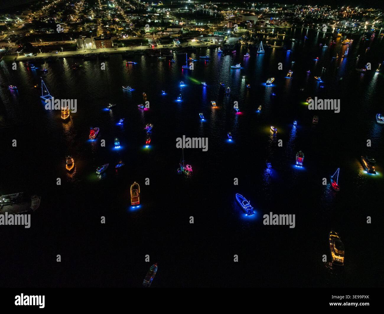 Luftaufnahme von Booten, die mit leuchtenden Neonlichtern im Hafen der Halbinsel Yucatan bei Nacht beleuchtet werden, mit Stadtlichtern im Hintergrund Yucatan, Stockfoto