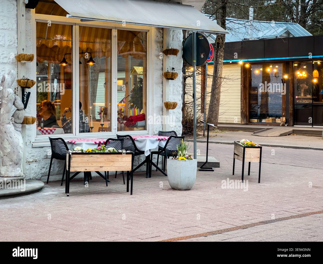 Jurmala, Lettland - 29. März 2026: Sitzbereich im Freien außerhalb der Saison mit Tischen, die mit Blumen geschmückt sind, vor einem lokalen Restaurant, das eine Dekora zeigt Stockfoto