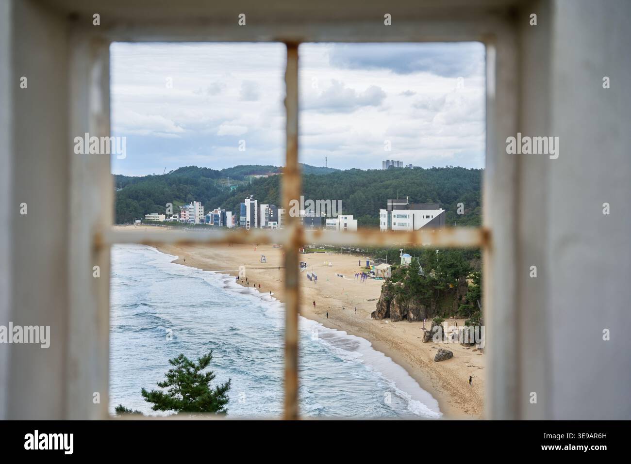 Fotos von Samcheok Beach unter bewölktem Himmel. Kreative Rahmen durch ein rostiges Fenster und eine weite Landschaftsaufnahme halten die nostalgische Küstenstimmung fest. Stockfoto