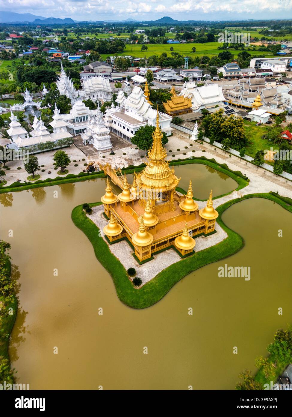 Blick aus der Vogelperspektive auf den reich verzierten goldenen Ganesha-Schrein und die weißen Tempelgebäude des Wat Rong Khun, umgeben von einem Teich und üppigem Grün in Pa O Don Chai, C Stockfoto