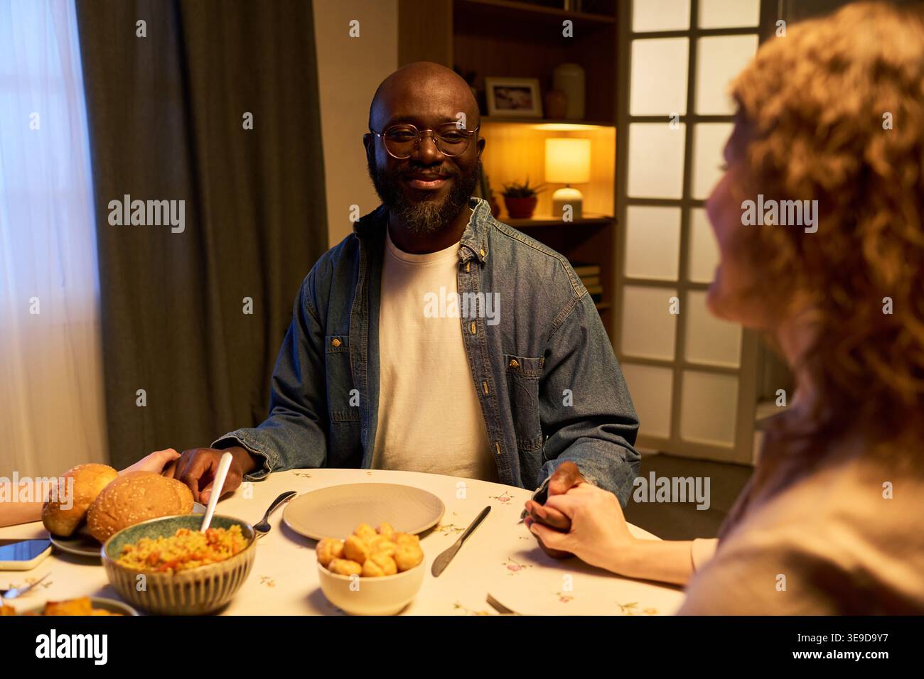 Schwarzer Mann, der ein Abendessen mit seinem Partner teilt, Hände am Tisch hält und während eines intimen Gesprächs lächelt. Ideal für Beziehungen, Familienleben, gemeinsames Marketing Stockfoto