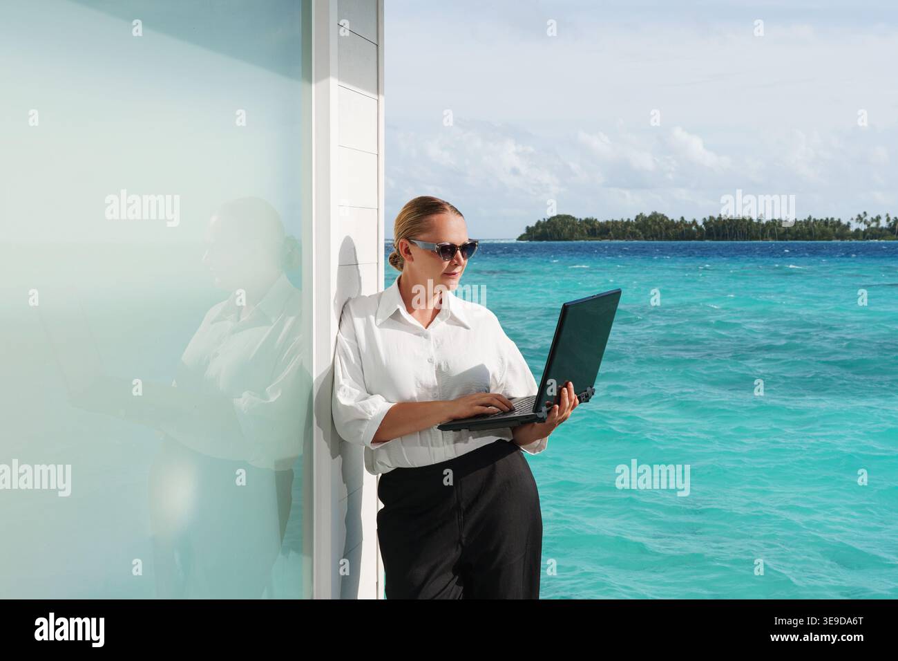 Lächelnde, erfolgreiche Frau mit Laptop an einem schönen, sonnigen Strand. Erfolg. Flexible Fernarbeit, Konzept der Vereinbarkeit von Beruf und Privatleben für Frauen. Stockfoto