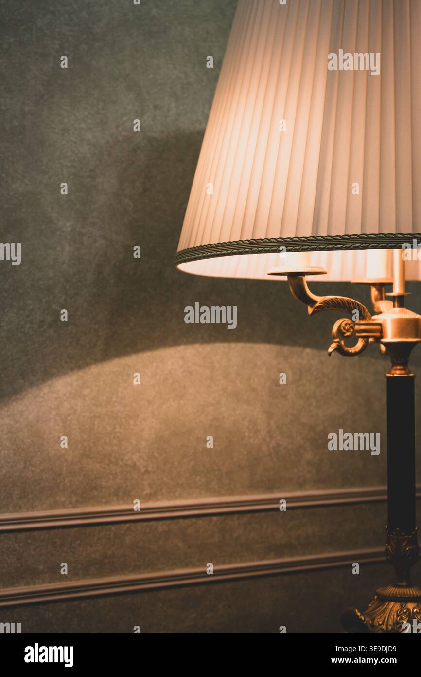 Altmodische Lampe mit Lampenschirm auf einem Tisch. Hotelzimmer-Design. Gemütlicher Heimstil. Klassisches Home-Design. Die Schlafzimmerlampe steht abends auf dem Tisch. Stockfoto
