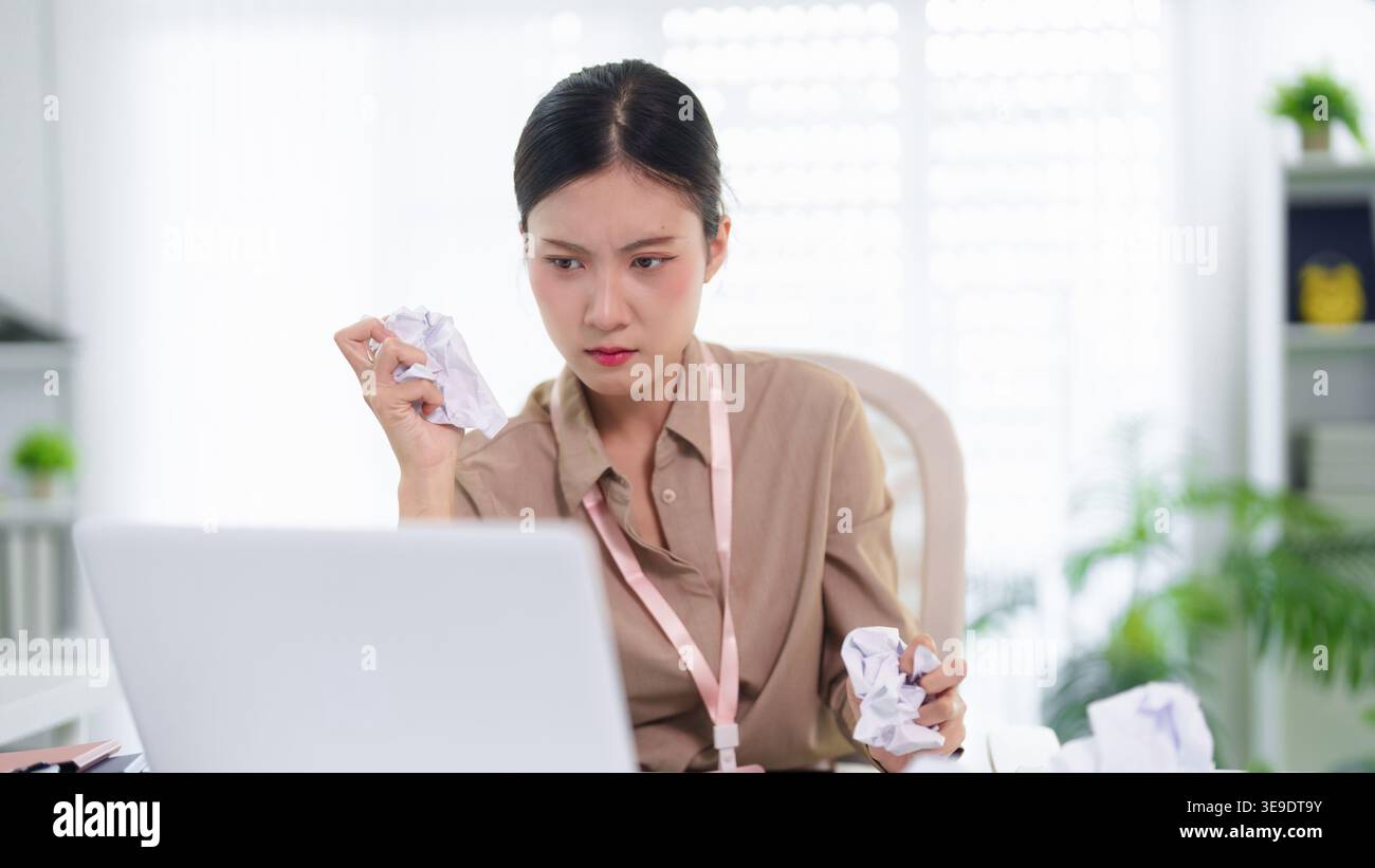 Junge asiatische Geschäftsfrau fühlt sich gestresst frustriert zerknittert Papier arbeitet Laptop Computer moderner Büroarbeitsplatz Stockfoto