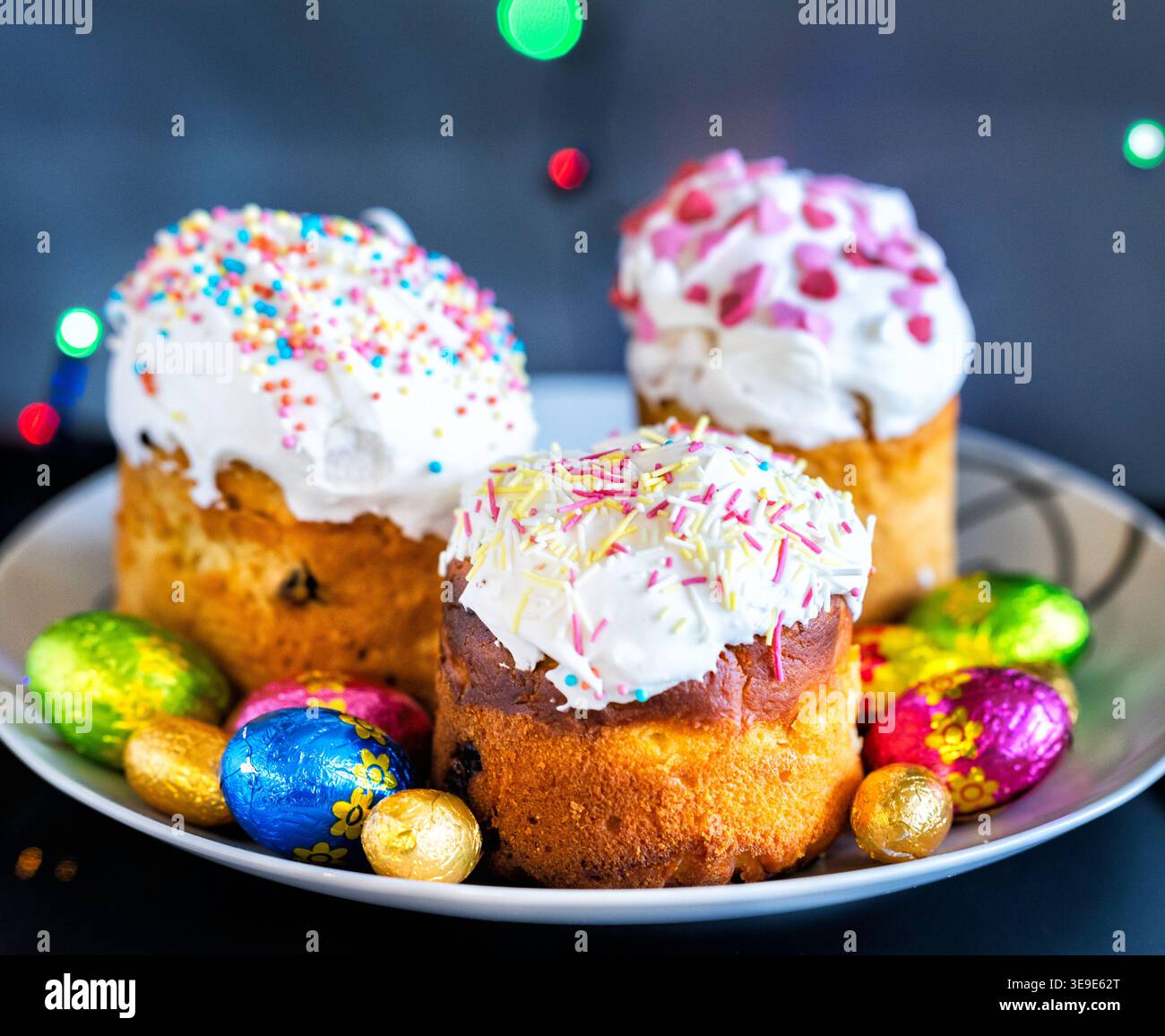 Ein Nahfoto mit drei traditionellen Osterkulich-Kuchen, die mit weißer Glasur und bunten Streuseln verziert sind. Sie ruhen auf einem Tisch, umgeben Stockfoto