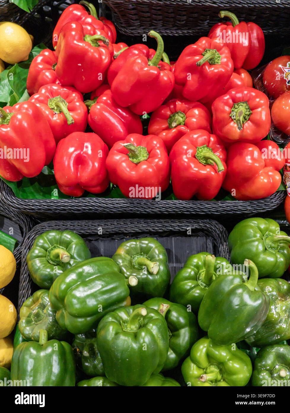 Lebendige Präsentation frischer, glänzender roter und grüner Paprika, die in schwarzen gewebten Körben im Einzelhandel oder auf einem Bauernmarkt angeordnet sind. Stockfoto