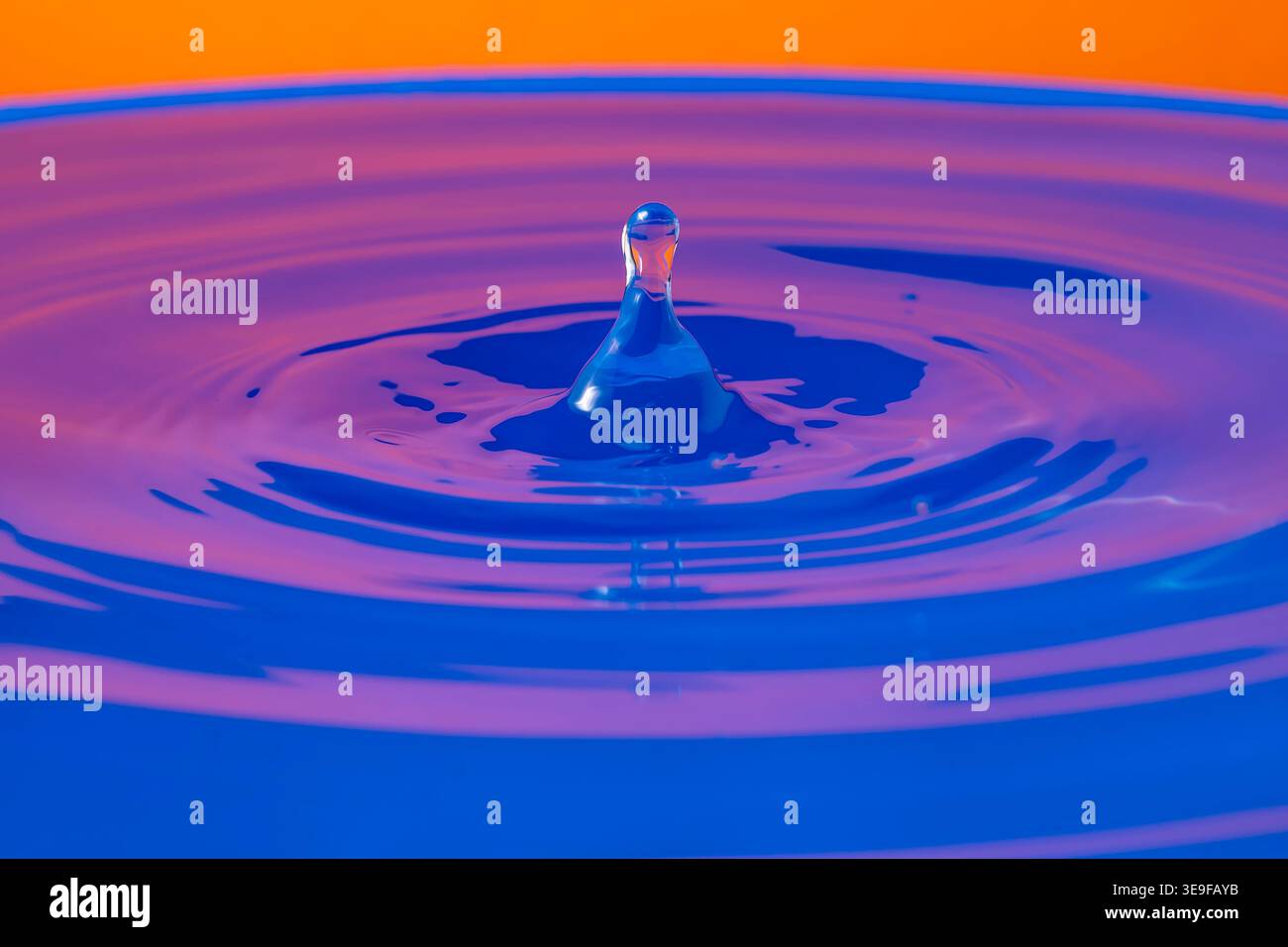 Das Abprallen eines Tropfens auf einer Oberfläche aus farbenfrohem Wasser mit spiegelnden Reflexen Stockfoto