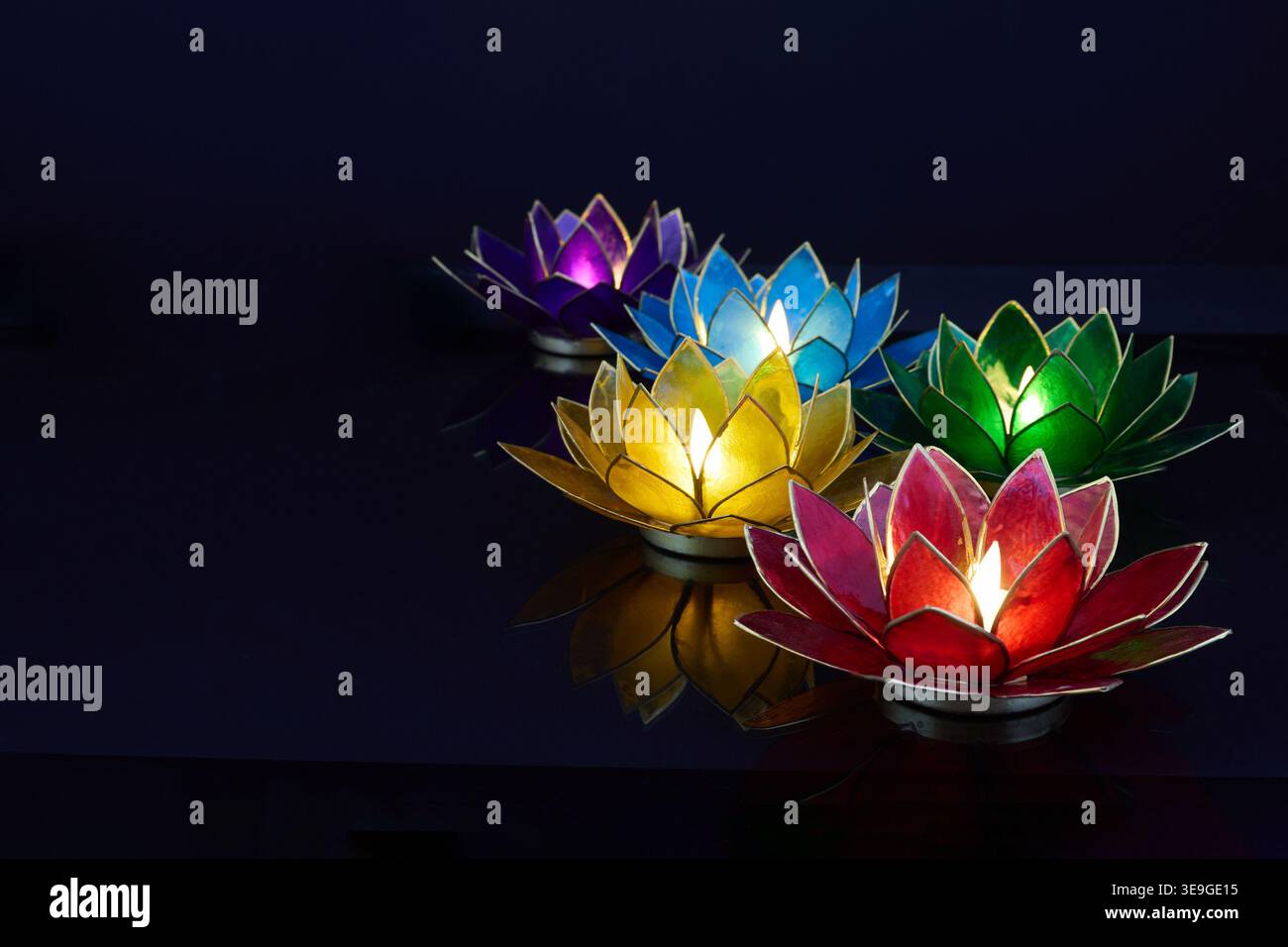 Vesak. Farbenfrohe Lotusblüten-Teelicht-Kerzen, die in dunklem Wasser leuchten Stockfoto