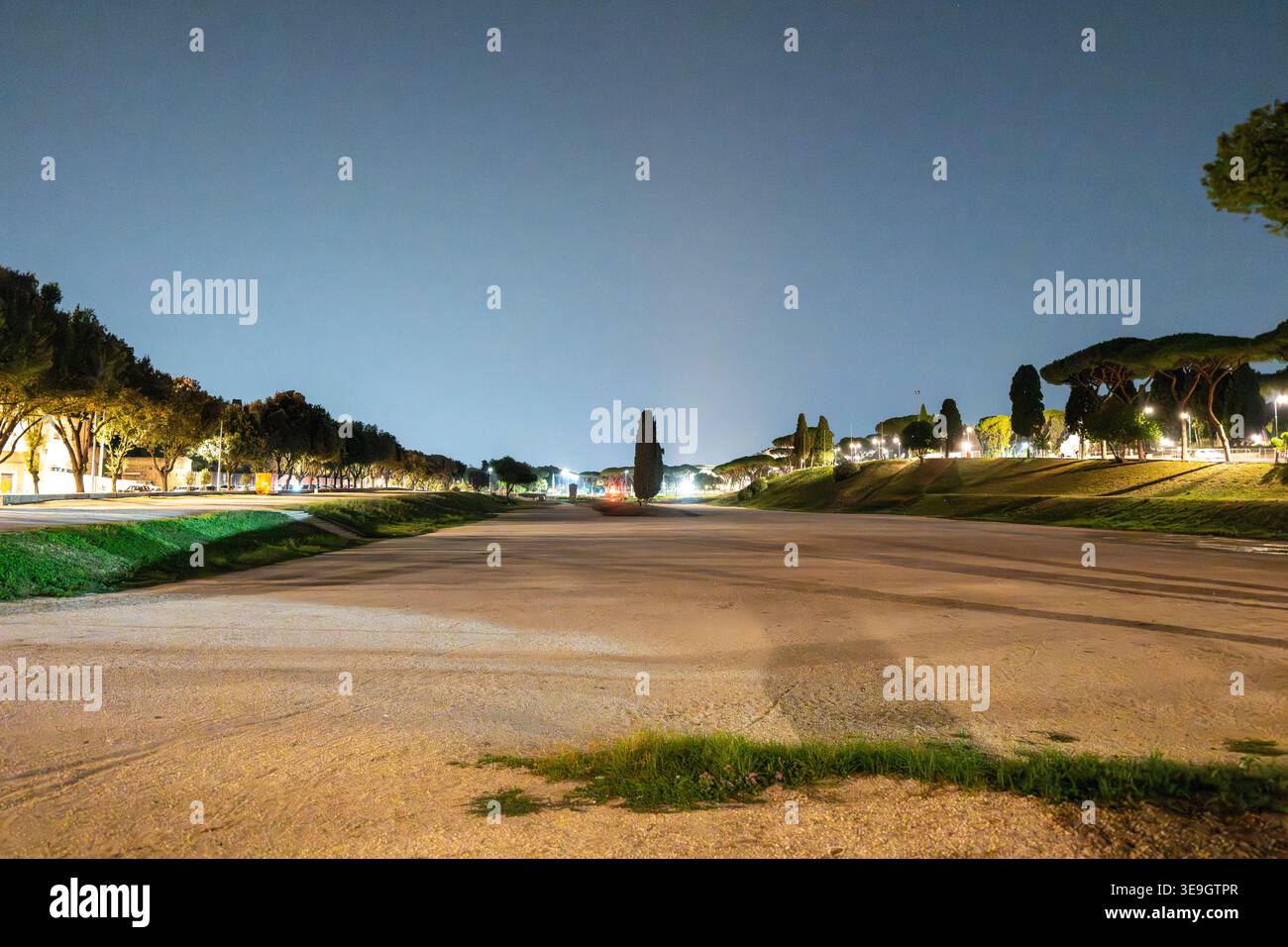 Nächtlicher Blick auf das offene Feld des Circus Maximus in Rom, mit beleuchteten Bäumen und fernen Lichtern der Stadt, die den alten römischen Wagenrennstand markieren Stockfoto
