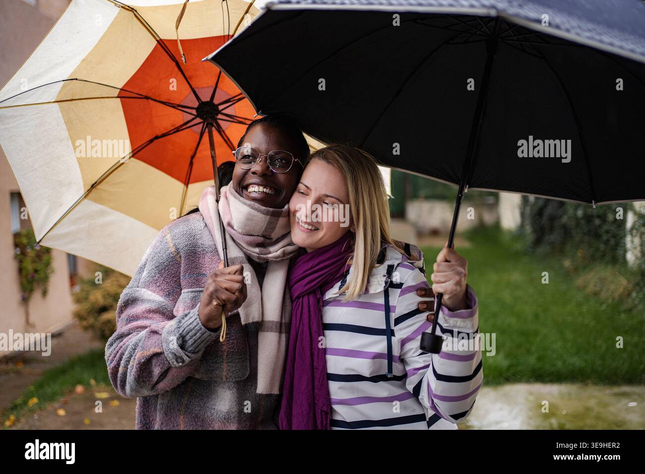 Verschiedene Freundinnen lächelnd und halten Regenschirme, die im Regen stehen Stockfoto