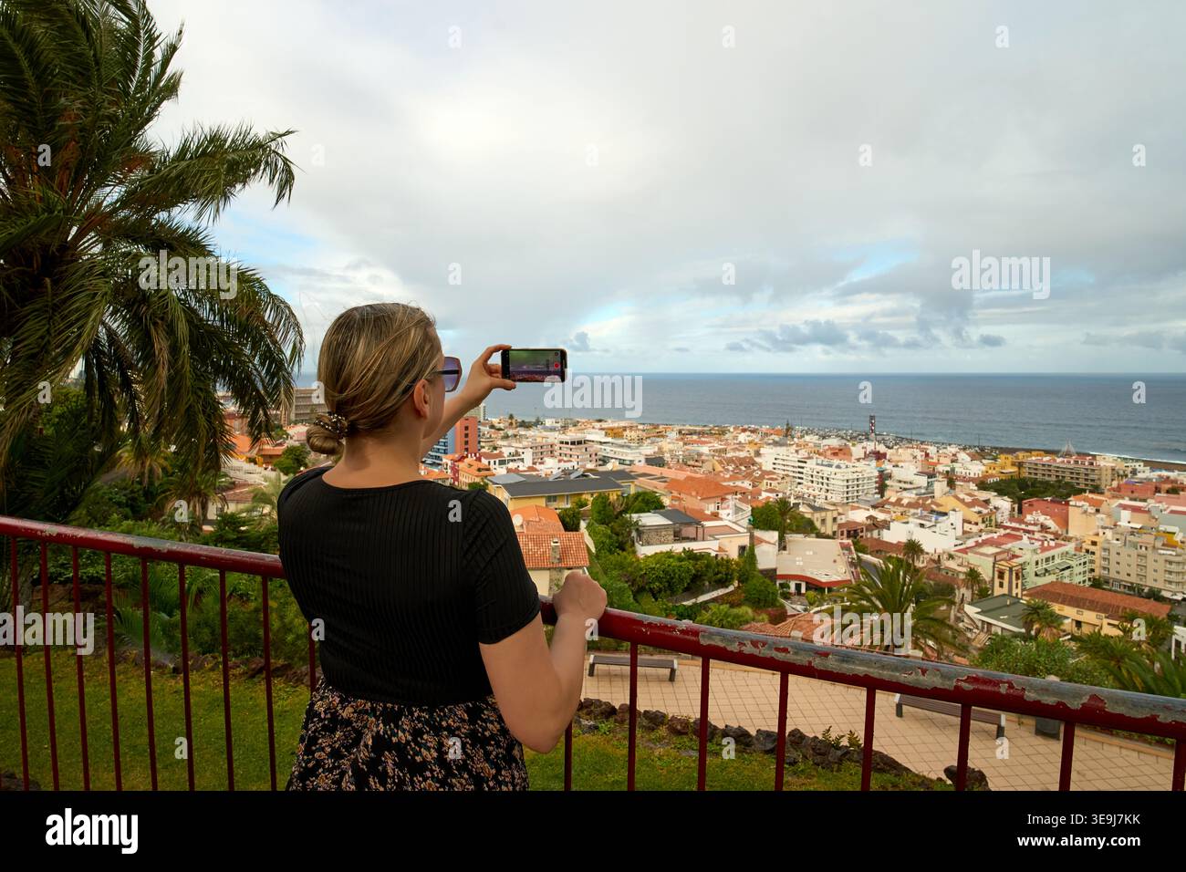 Frau, die mit ihrem Smartphone ein Foto von der Panoramablick auf die Stadt und das Meer von einem Aussichtspunkt in Puerto de la Cruz, Teneriffa, Kanarischen Inseln macht. Stockfoto