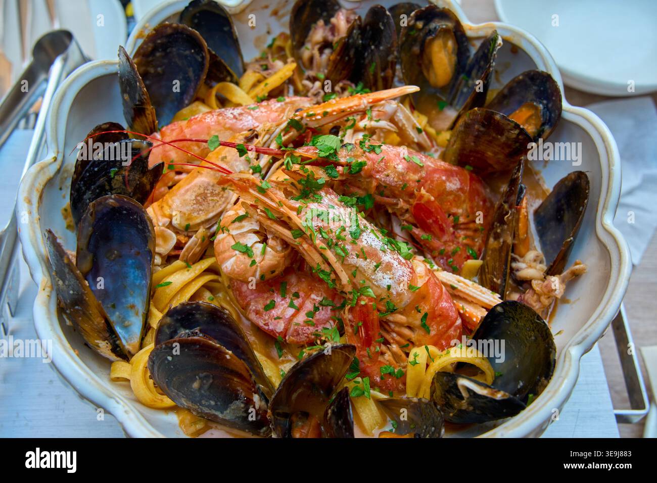 Köstliche Pasta mit Meeresfrüchten, großen Garnelen und Muscheln in einer Keramikschale. Traditionelle mediterrane Linguine mit Muscheln und frischen Kräutern. Stockfoto