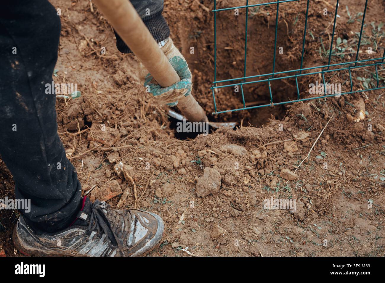 Arbeiter graben Boden mit einer Schaufel in der Nähe einer Metallkonstruktion, bereiten Boden für die Montage von Zaunzäunen, Bauverfahren im Freien und manuelle Arbeit vor. Stockfoto
