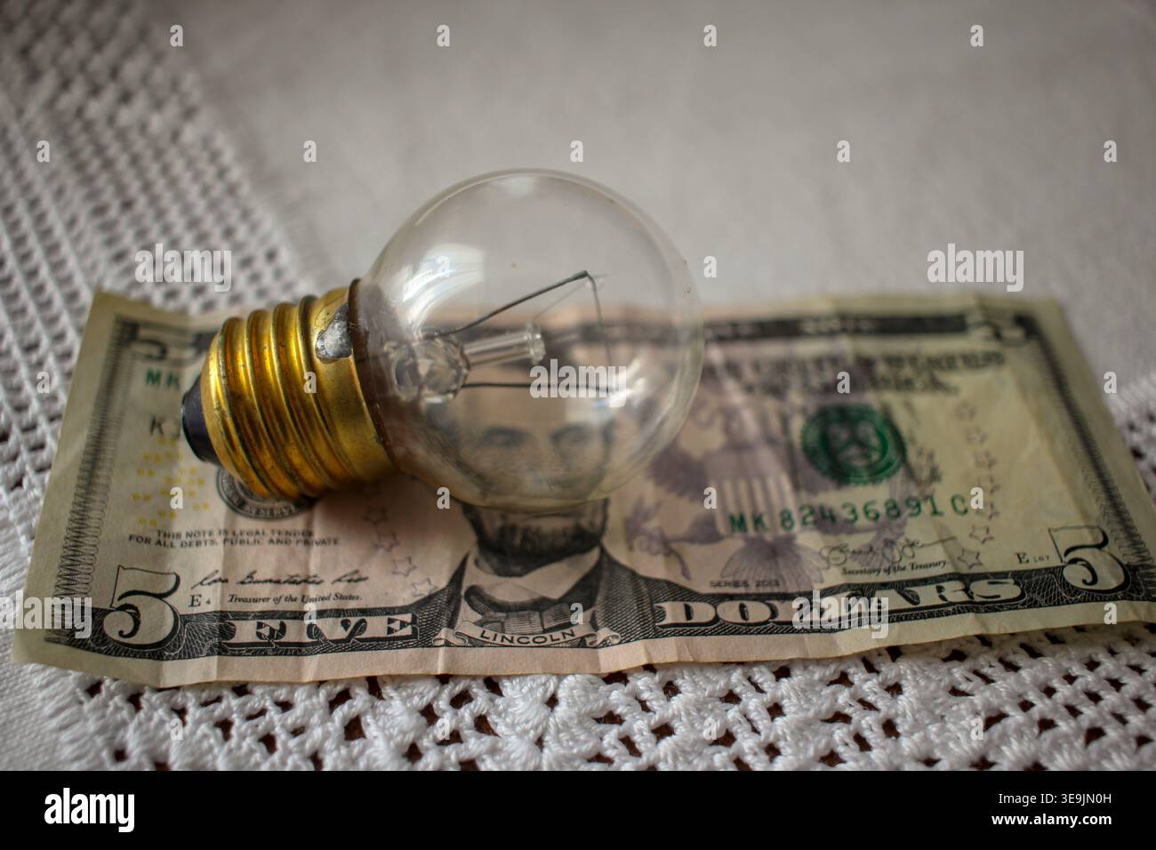 Nahaufnahme einer modernen Energiesparlampe neben einer Sparbank und einigen Münzen. Konzept zur Senkung der Stromrechnungen, Haushaltsführung, SZ Stockfoto