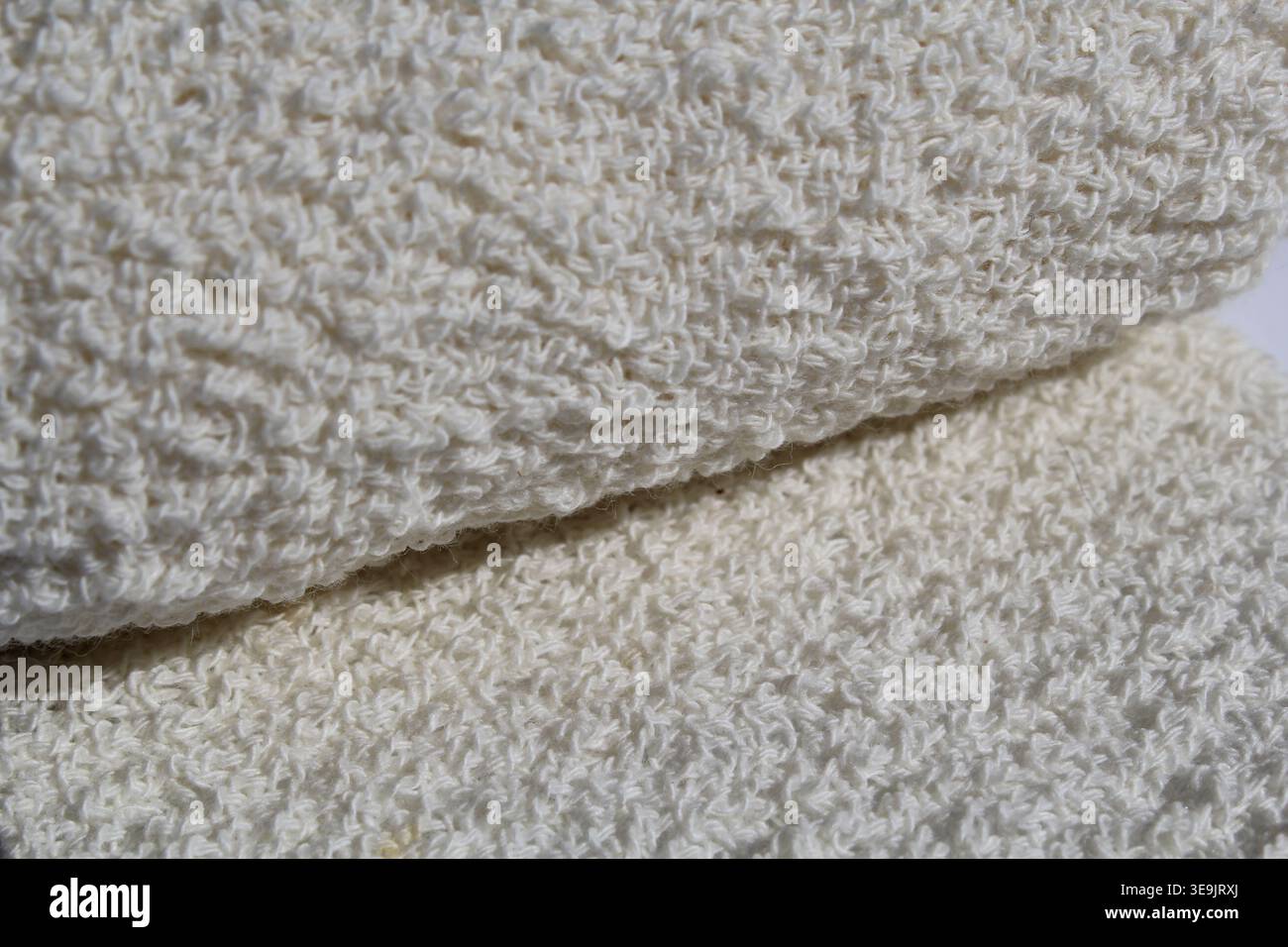 Nahaufnahme der Textur eines weichen, cremefarbenen gewebten Baumwollkrepbands, das über sich selbst gefaltet ist Stockfoto