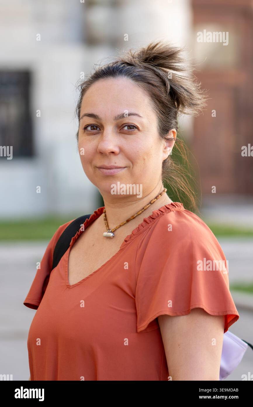 Weibliches Porträt draußen bei Tageslicht mit verschwommenem urbanem Hintergrund. Stockfoto
