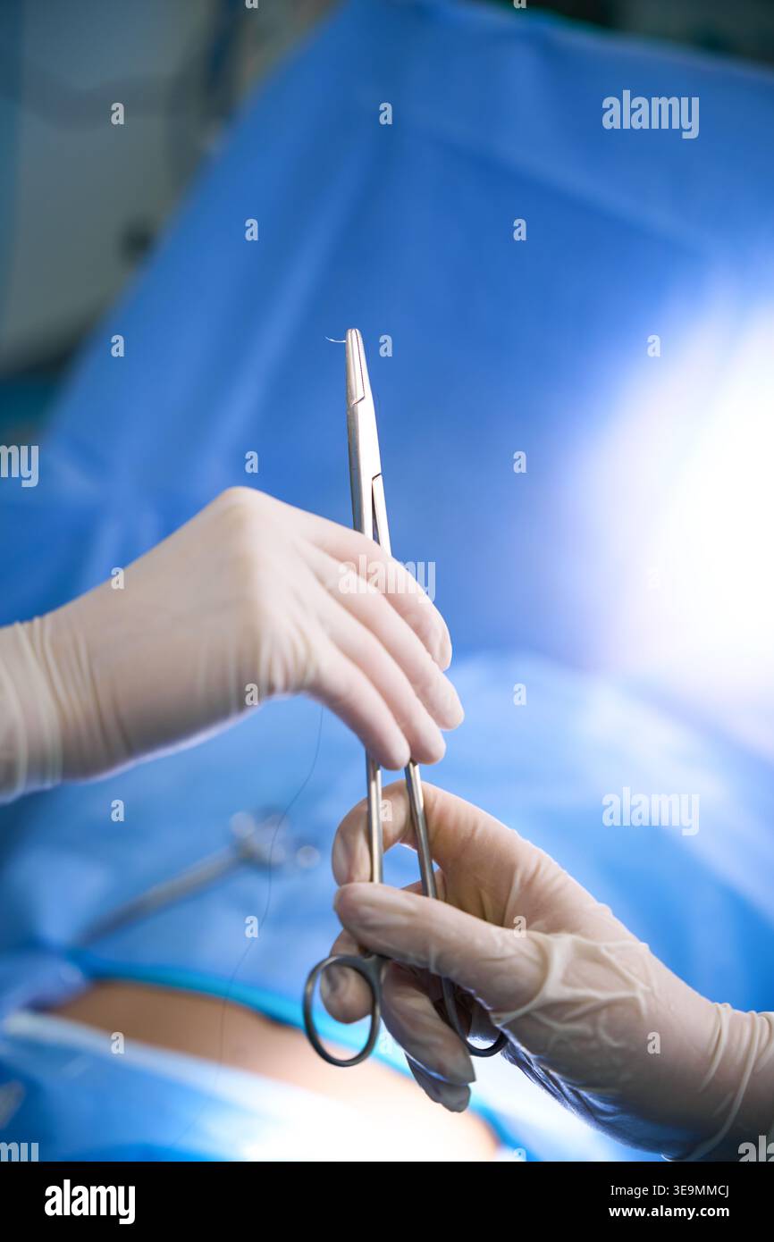 Zwei Hände in weißen Handschuhen, die chirurgische Instrumente in Innenräumen halten Stockfoto