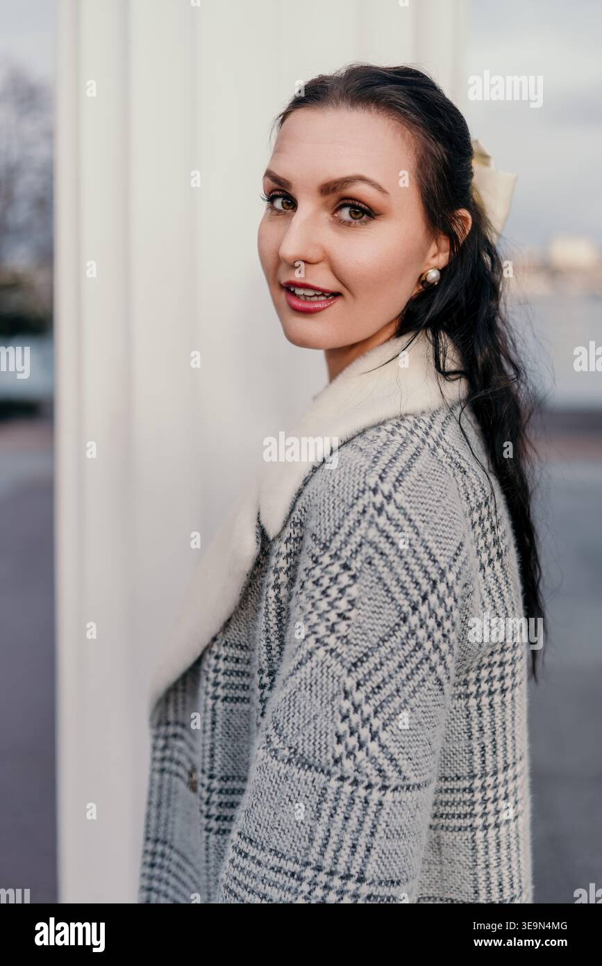 Frau Mantel Portrait junge Dame in grauer karierter Jacke mit weißem Kunstfellkragen, der draußen über die Schulter blickt Stockfoto