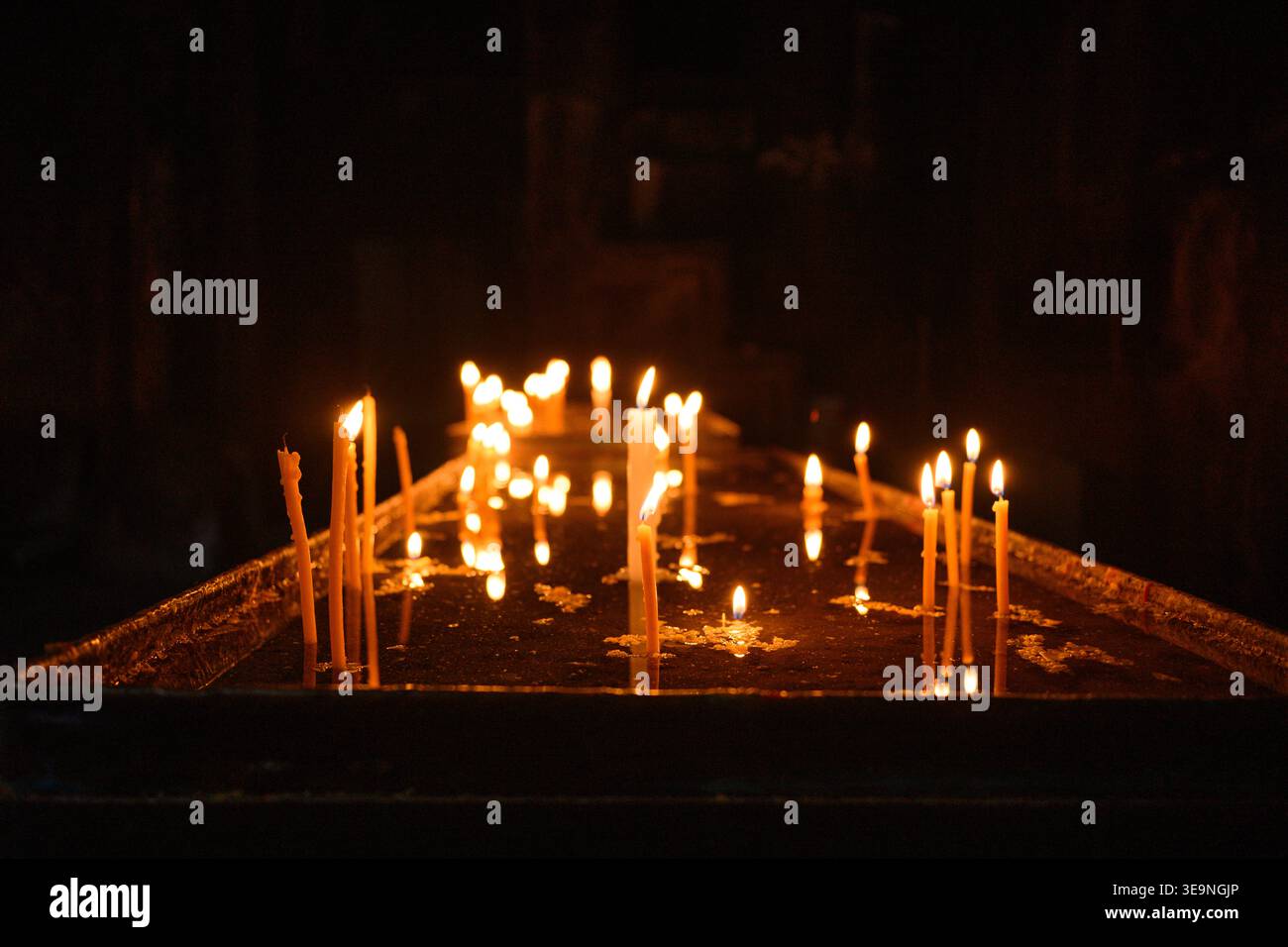 Viele Kerzen leuchten in der Dunkelheit warm. Die Flammen flackern sanft auf der Holzoberfläche. Kerzenhalter stehen aufrecht mit sanftem Licht. Warmes Ambiente geschaffen Stockfoto