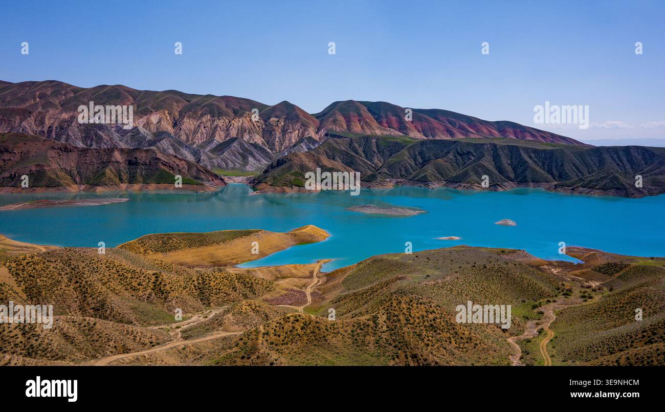 Blick aus der Vogelperspektive auf den türkisfarbenen See, umgeben von zerklüfteten Bergen. Berge zeigen erdige Rot- und Brauntöne. Das Wasser reflektiert den klaren blauen Himmel darüber. Querformat Stockfoto