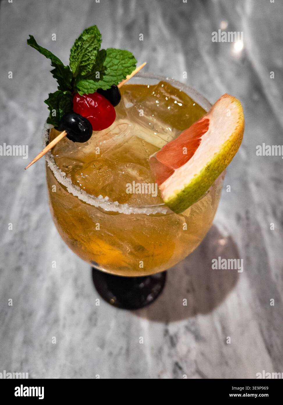 Ein lebendiger Zitruscocktail in einem gekühlten Glas mit gesalzenem Rand, garniert mit frischer Minze, einer Kirsche, Heidelbeeren und einer Scheibe Grapefruit. Stockfoto