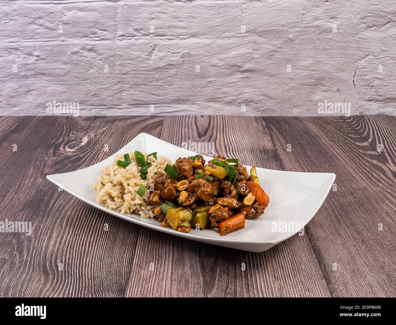 Ein gesundes, hausgemachtes Hühnchen-Reis-Gericht mit Gemüse, serviert auf einem weißen Teller auf einem rustikalen Holztisch Stockfoto
