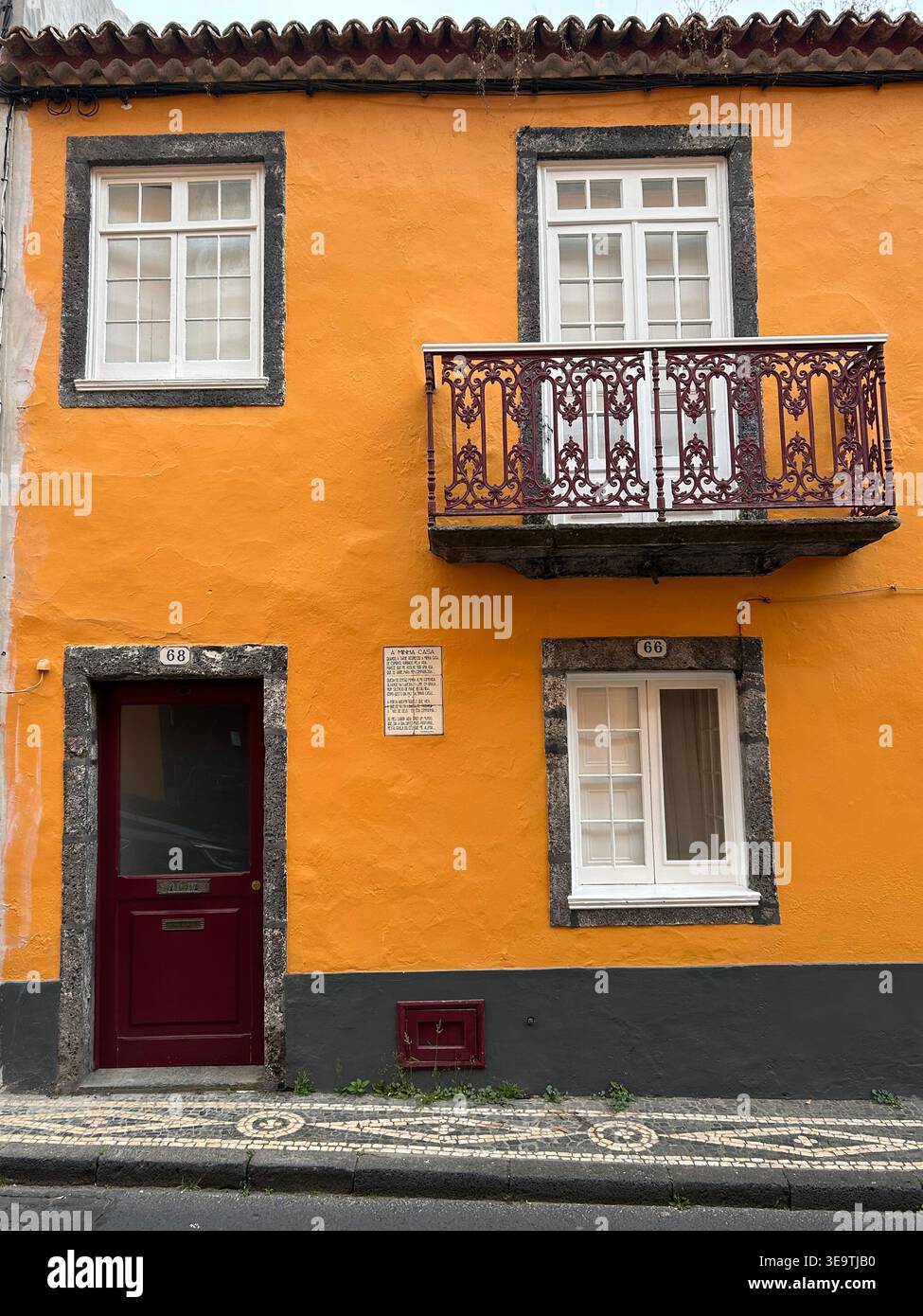 Orangenhaus in Ponta Delgada, Azoren, Portugal, mit Balkon und burgunderroter Tür, die traditionelle azoranische Architektur und Inselcharme zeigt - Smartphone-aufgenommenes Stockfoto