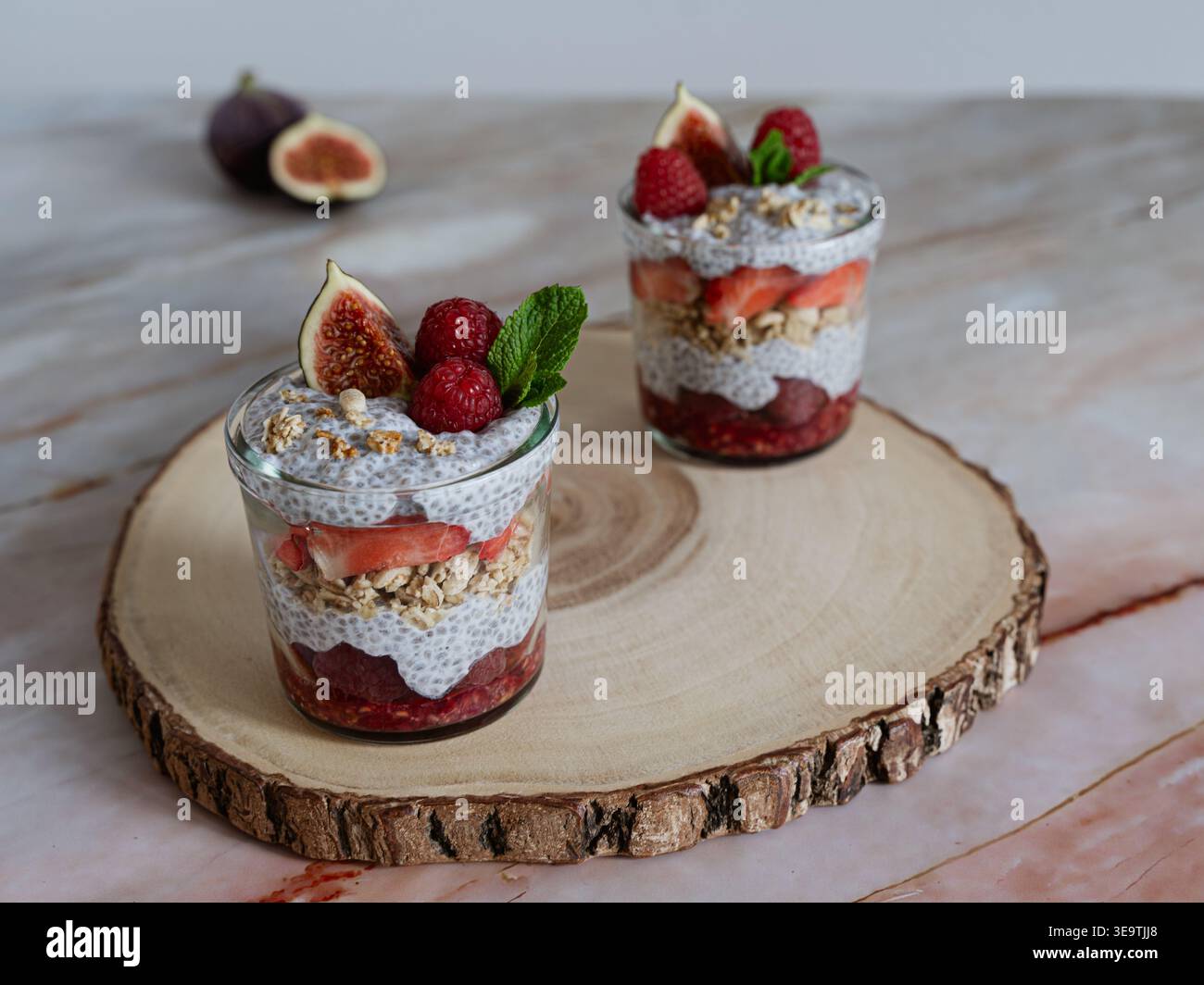 Vorderansicht der zweischichtigen Chia-Desserts mit Beeren und Müsli auf natürlichem Holzschnitt Stockfoto