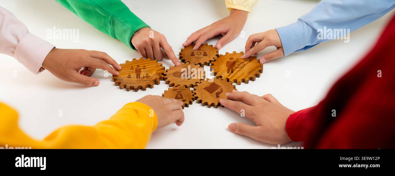 Dieses Bild zeigt verschiedene Hände, die nach hölzernen Zahnrädern greifen und Teamarbeit und Zusammenarbeit in einem kreativen Arbeitsbereich hervorheben – perfekt für Projekte Stockfoto