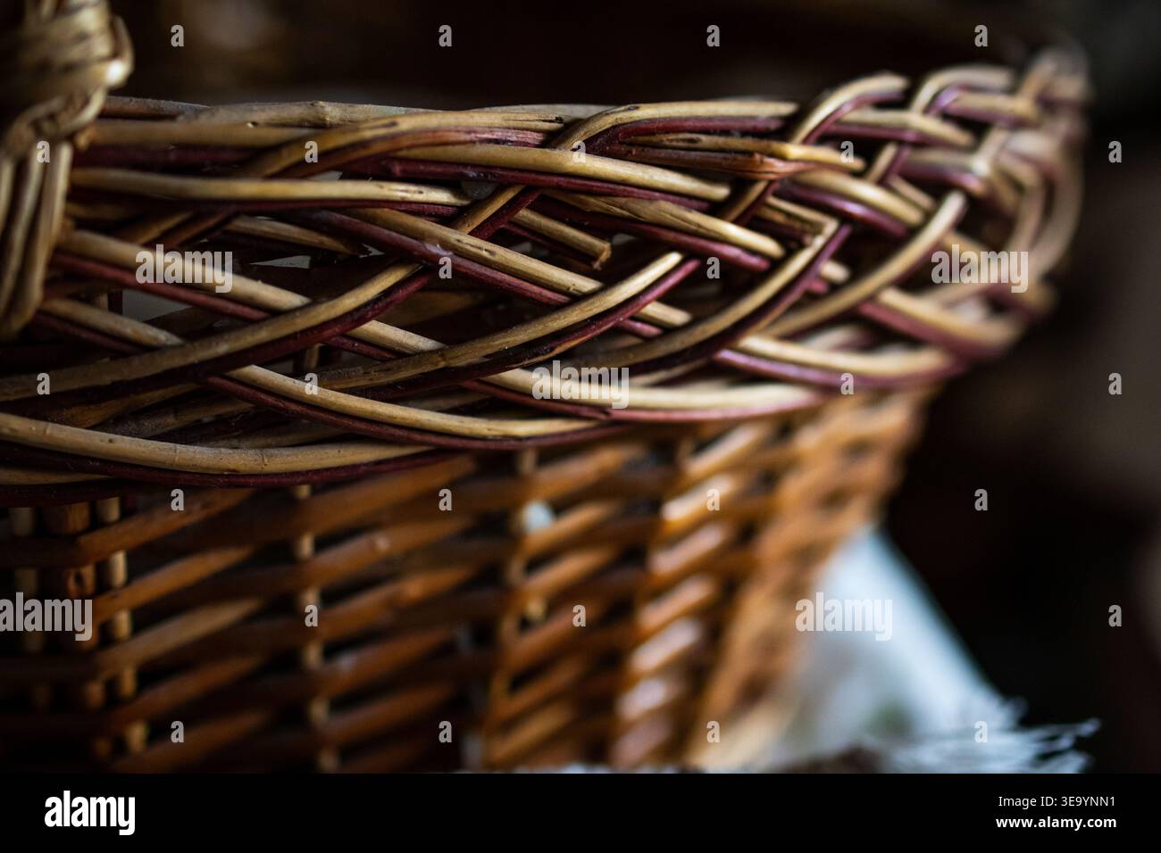 Detaillierter Blick auf einen gewebten Korb mit verzierten geflochtenen Kanten und Erdtönen. Der flache Fokus hebt die taktilen Fasern und die traditionelle Handwerkskunst hervor Stockfoto