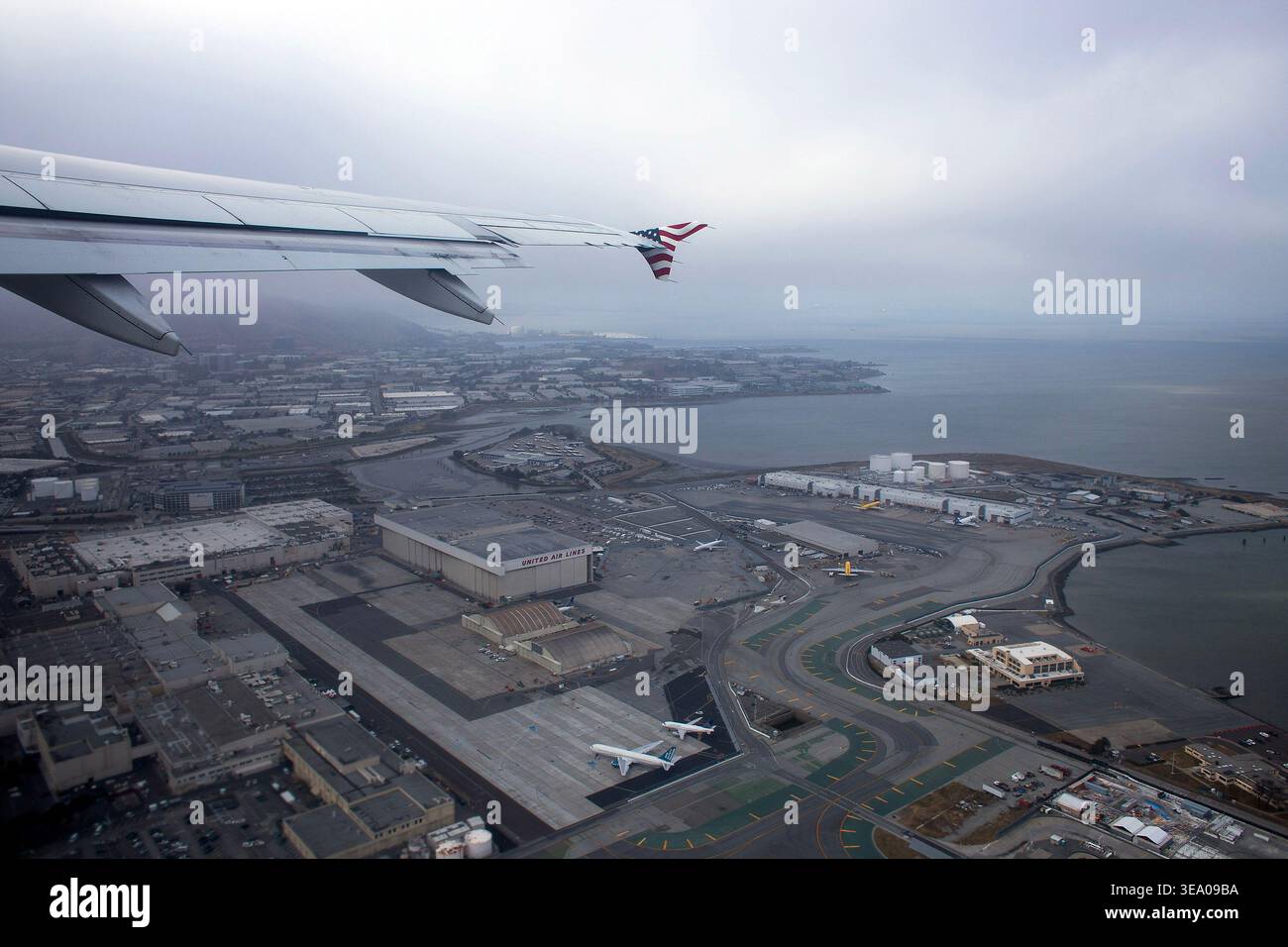 Ein Flugzeug fliegt über eine Stadt mit einem Hafen und Industriegebäuden darunter. Stockfoto