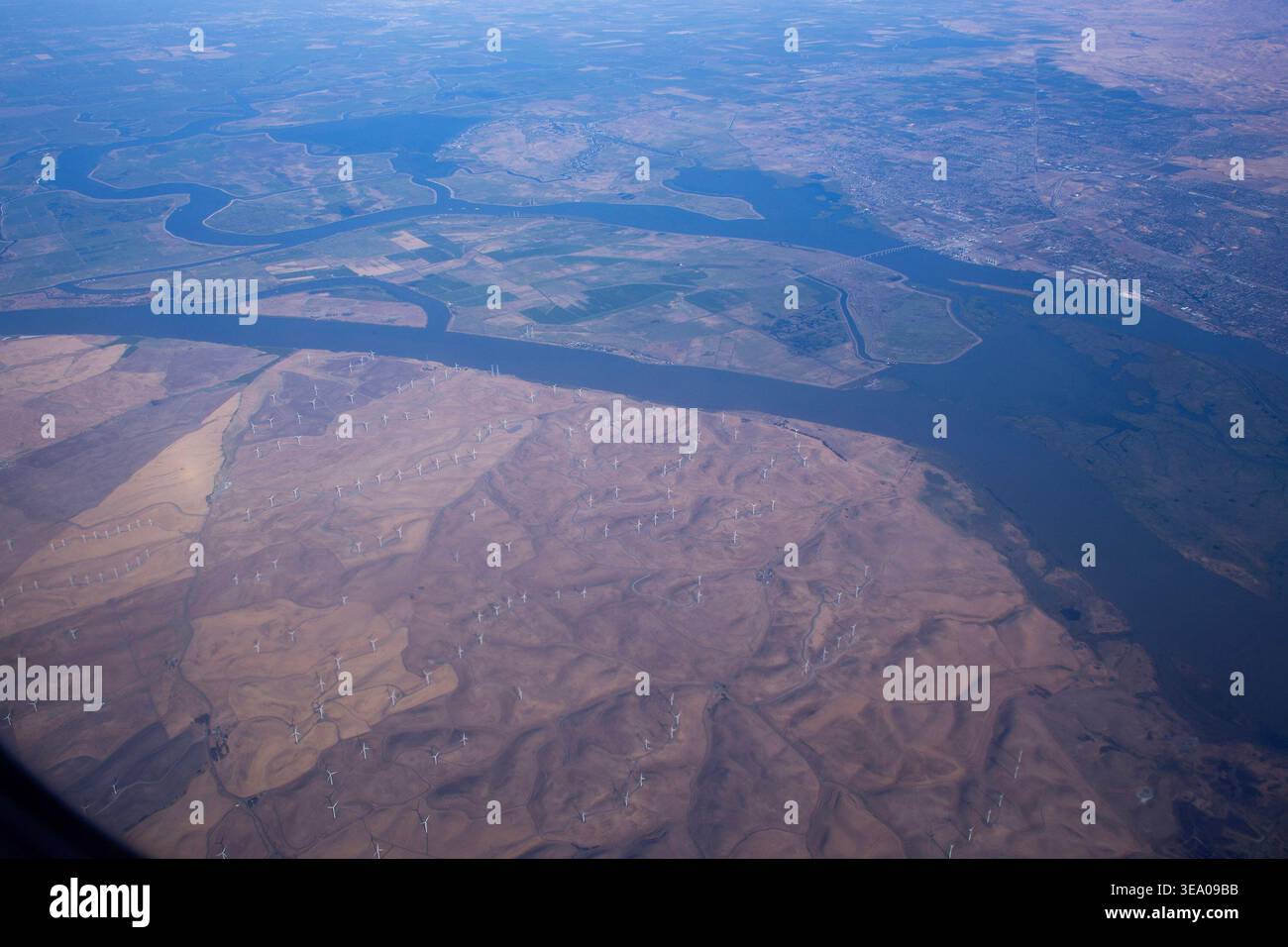 Aus der Vogelperspektive gewundene Flüsse, die durch trockenes Gelände fließen, mit sichtbaren Flussufern und entfernten städtischen Gebieten. Stockfoto