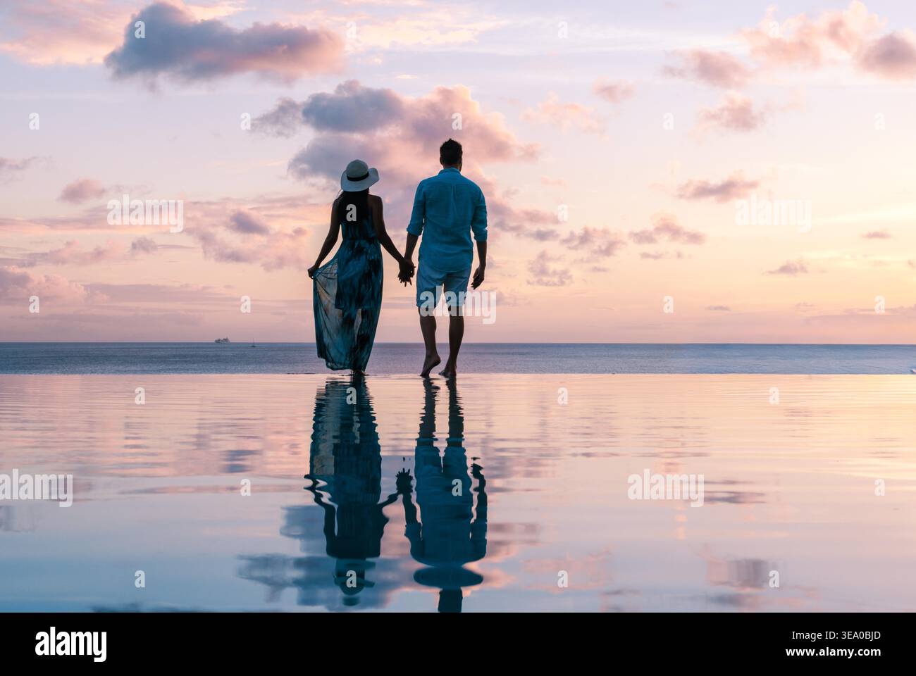 Ein Paar genießt einen romantischen Spaziergang entlang der glitzernden Küste von Saint Lucia bei Sonnenuntergang. Die leuchtenden Farben des Himmels spiegeln sich wunderbar auf dem ruhigen Wasser wider und schaffen eine ruhige Atmosphäre. Stockfoto