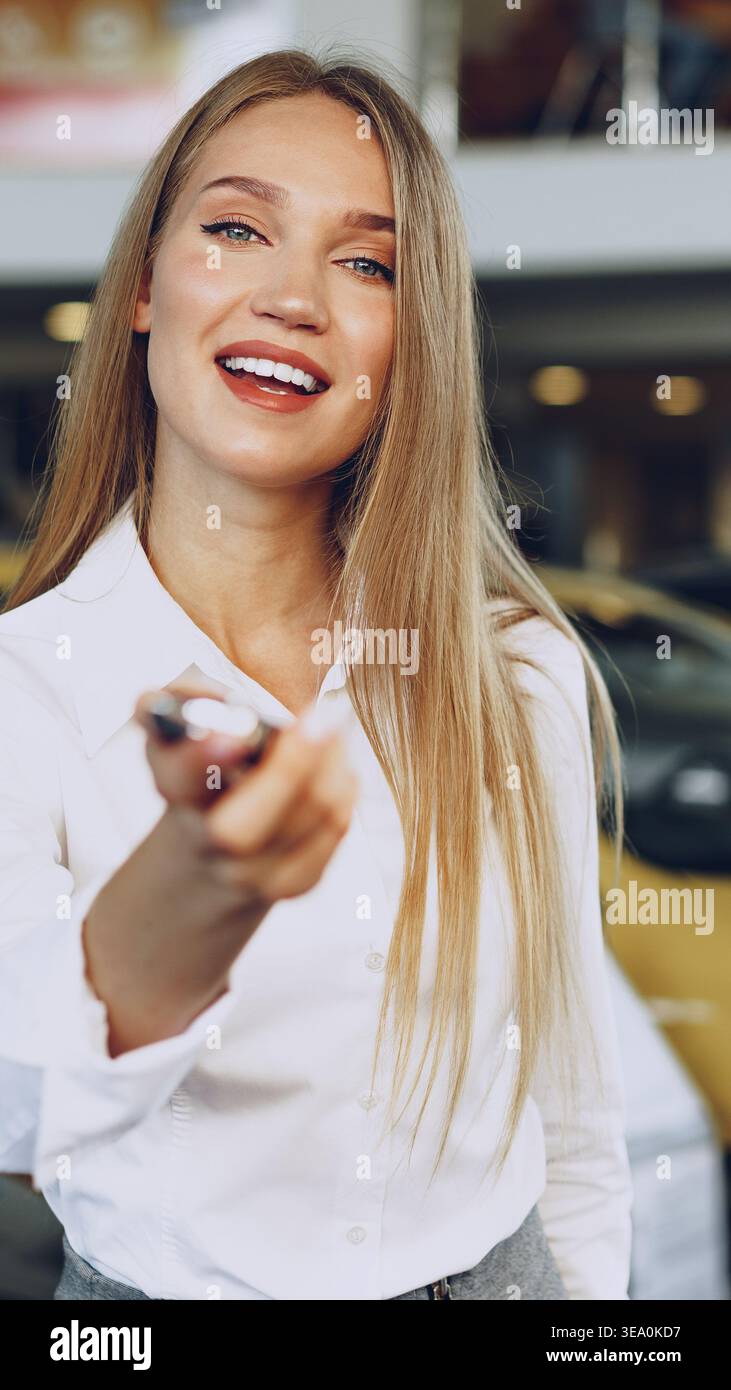 Frau lächelt tagsüber, während sie Autoschlüssel in einem Händlerbetrieb hält Stockfoto
