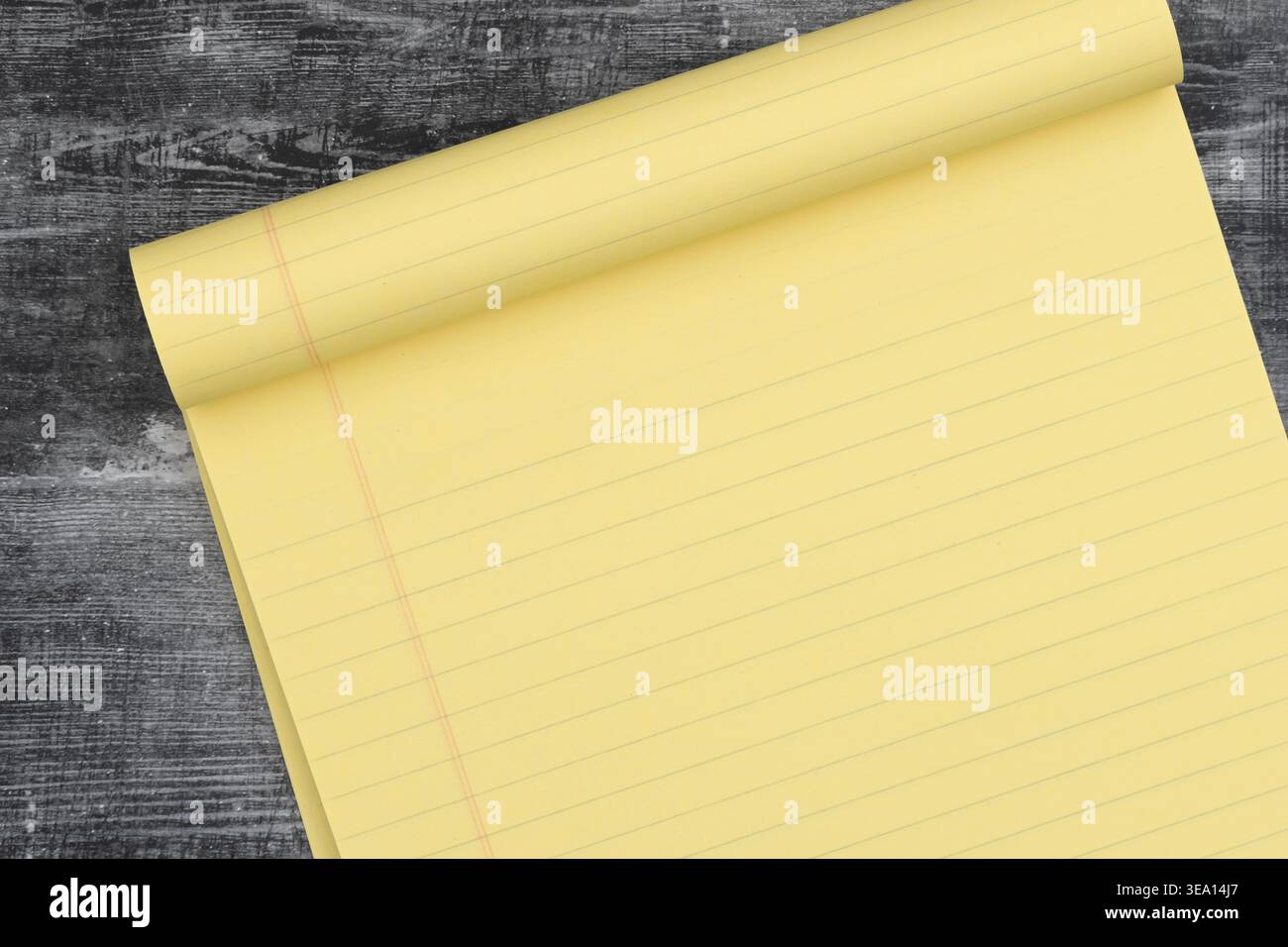 Gelbes Notizbuch aus Legal auf dunklem rustikalem Holztisch, auf dem liniertes Papier für Notizen, Planung, Schreibtideen und Produktivität gezeigt wird. Stockfoto