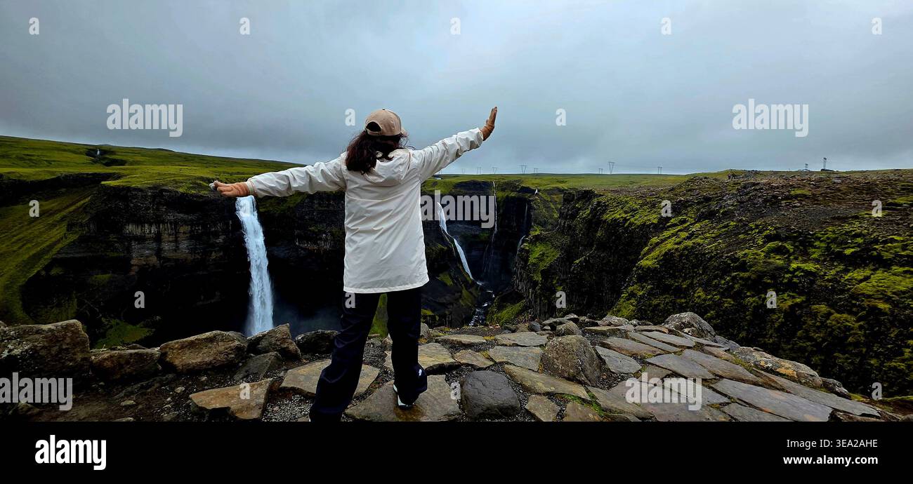 Frau steht am Rand der Klippe und beobachtet Haifoss in Island - Smartphone-aufgenommenes Stockfoto