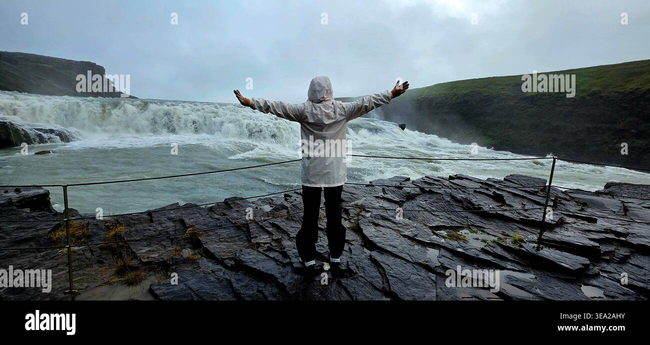 Frau, die mit offenen Händen steht und Gullfoss in Island beobachtet - Smartphone-aufgenommenes Stockfoto