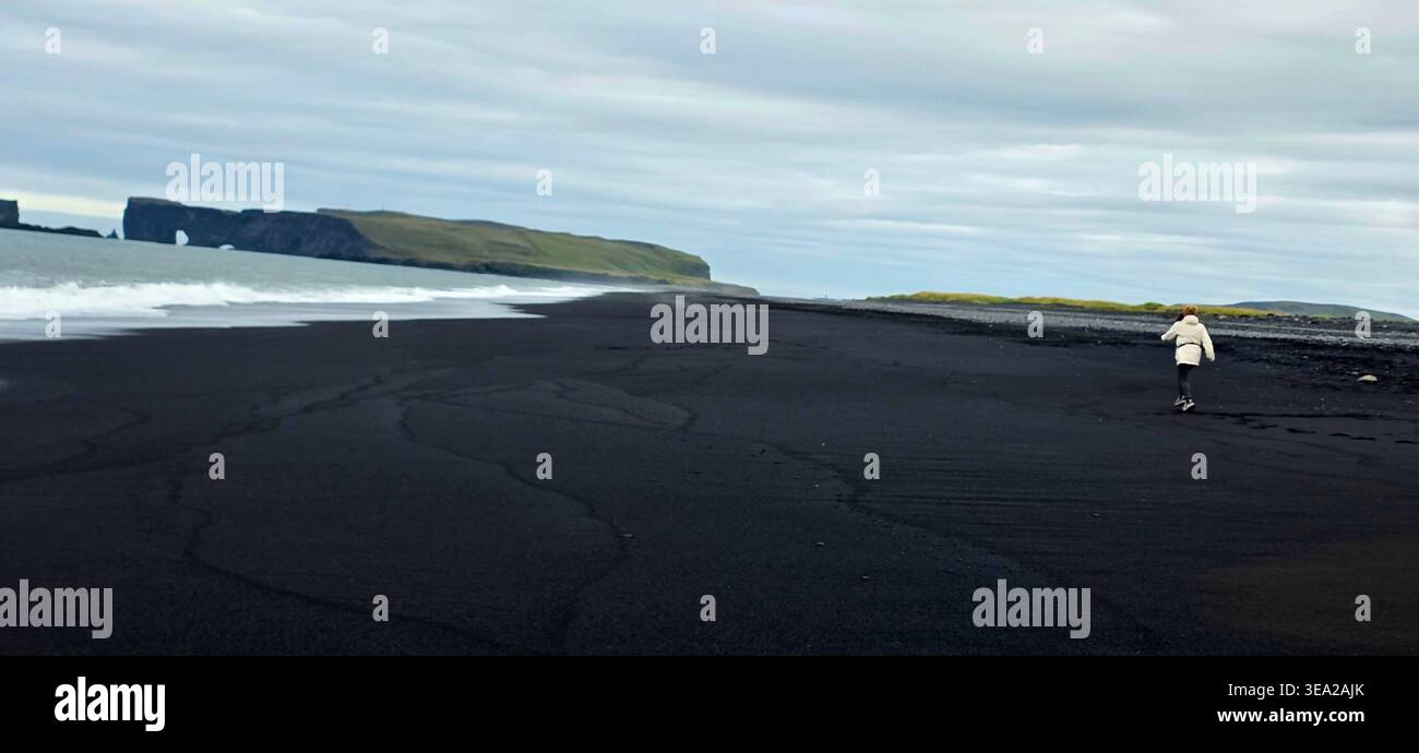 Frau mit weißer Jacke, die am Strand von Reynisfjara läuft - Smartphone-aufgenommenes Stockfoto